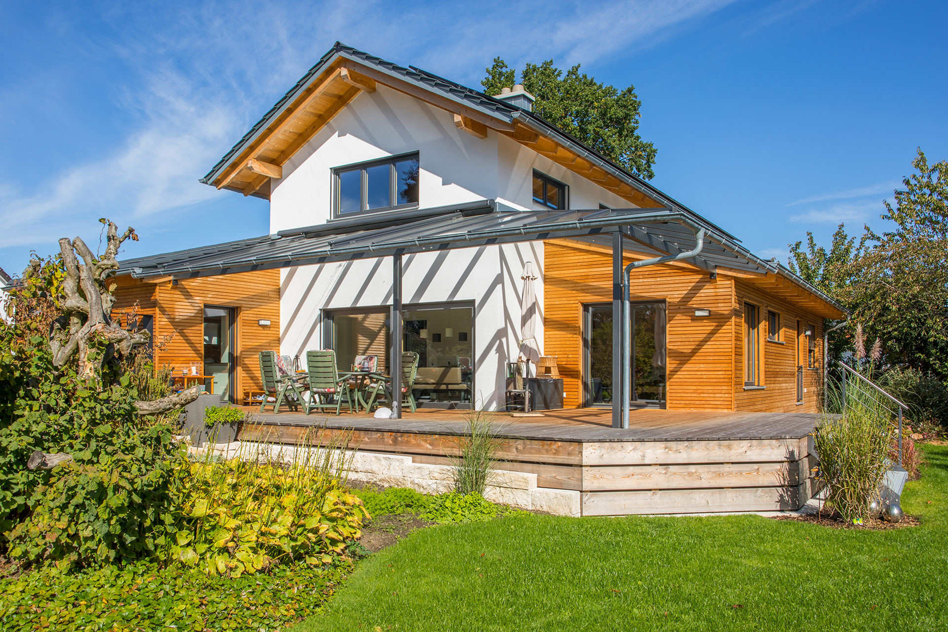 Das Holzhaus ist teilweise verputzt und hat einen überdachten Übereck-Erker mit einer horizontalen Holzfassade. Auf der anderen Seite ist eine überdachte Terrasse. © Brunthaler Naturhausmanufaktur