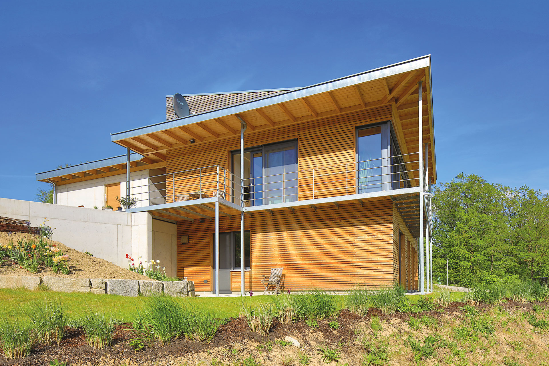 Modernes Holzhaus in Hanglage mit Übereck-Balkon und Pultdach. Die horizontal laufende Holzfassadenbretter sind unbehandelt. © Brunthaler Naturhausmanufaktur