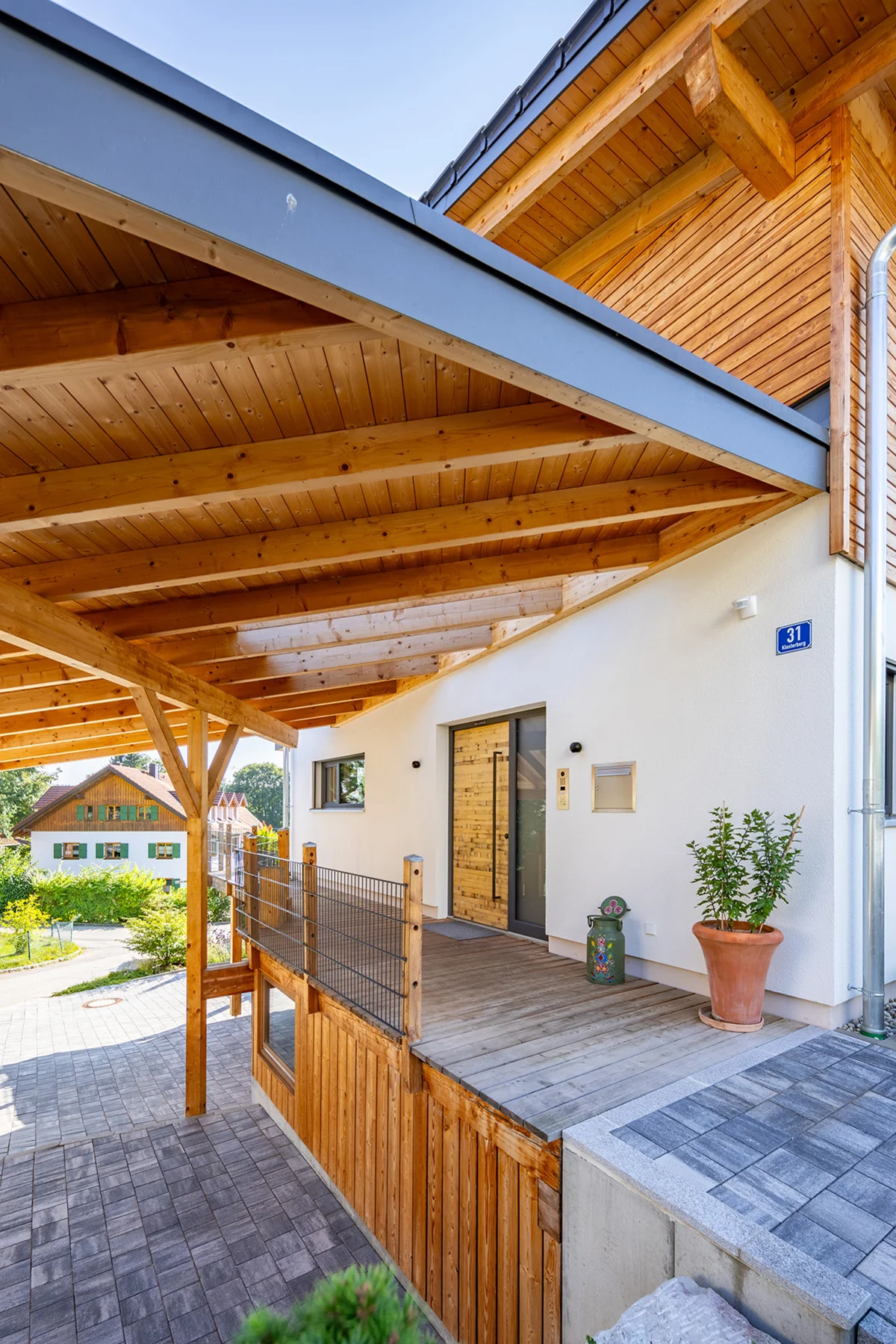 Der Eingangsbereich des Holzhauses in Hanglage von Außen. Der umlaufende Balkon dient hier als Eingangsbereich, der großflächig überdacht ist und somit einen Carport bildet. © Brunthaler Naturhausmanufaktur