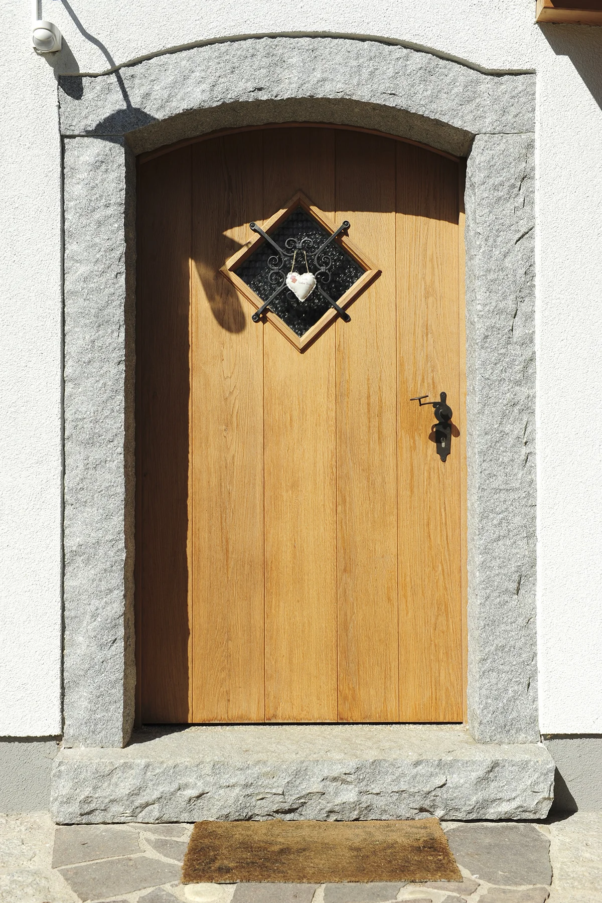 Eine Tür aus Holz umrandet mit Stein und einem kleinen Fenster. Verputzte Fassade. © Brunthaler Naturhausmanufaktur