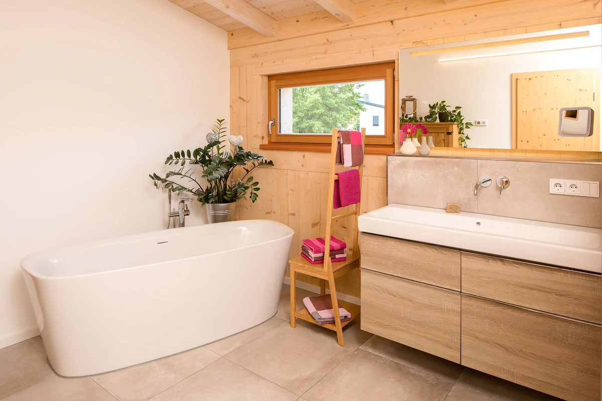 Badezimmer mit verputzter Wand und Holzwand, mit freistehender Badewanne, pinken Farbakzenten und einem großen Waschbecken. © Brunthaler Naturhausmanufaktur