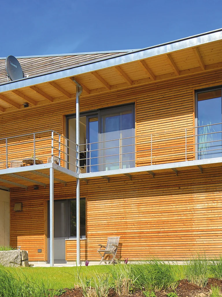 Modernes Holzhaus in Hanglage mit Übereck-Balkon und Pultdach. Die horizontal laufende Holzfassadenbretter sind unbehandelt. © Brunthaler Naturhausmanufaktur