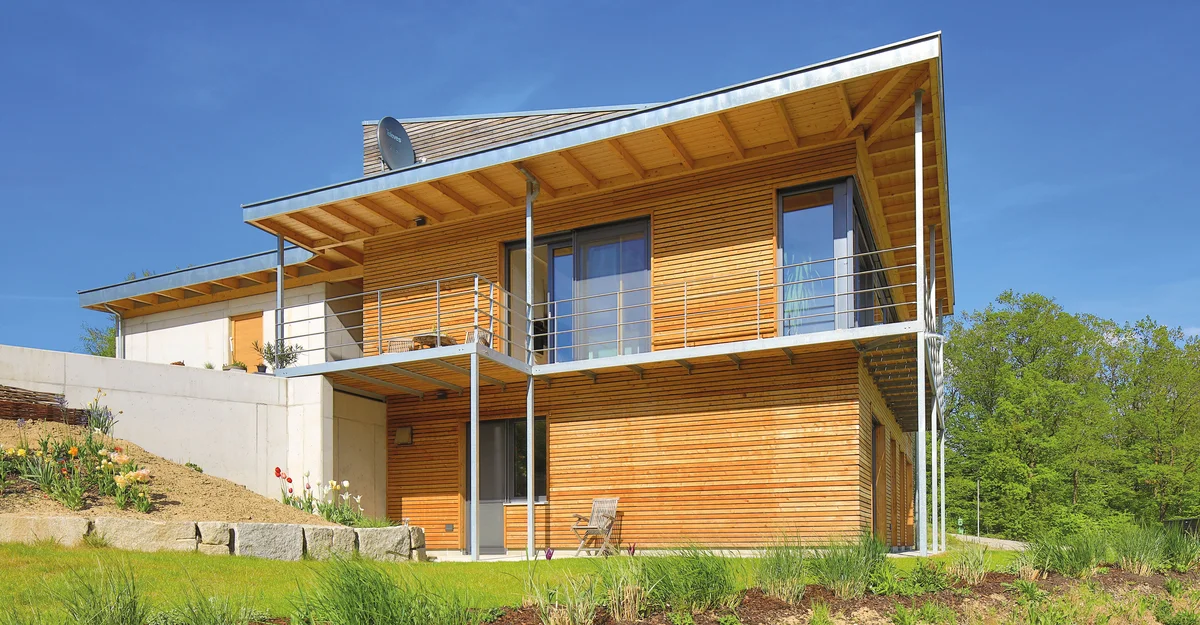 Modernes Holzhaus in Hanglage mit Übereck-Balkon und Pultdach. Die horizontal laufende Holzfassadenbretter sind unbehandelt. © Brunthaler Naturhausmanufaktur