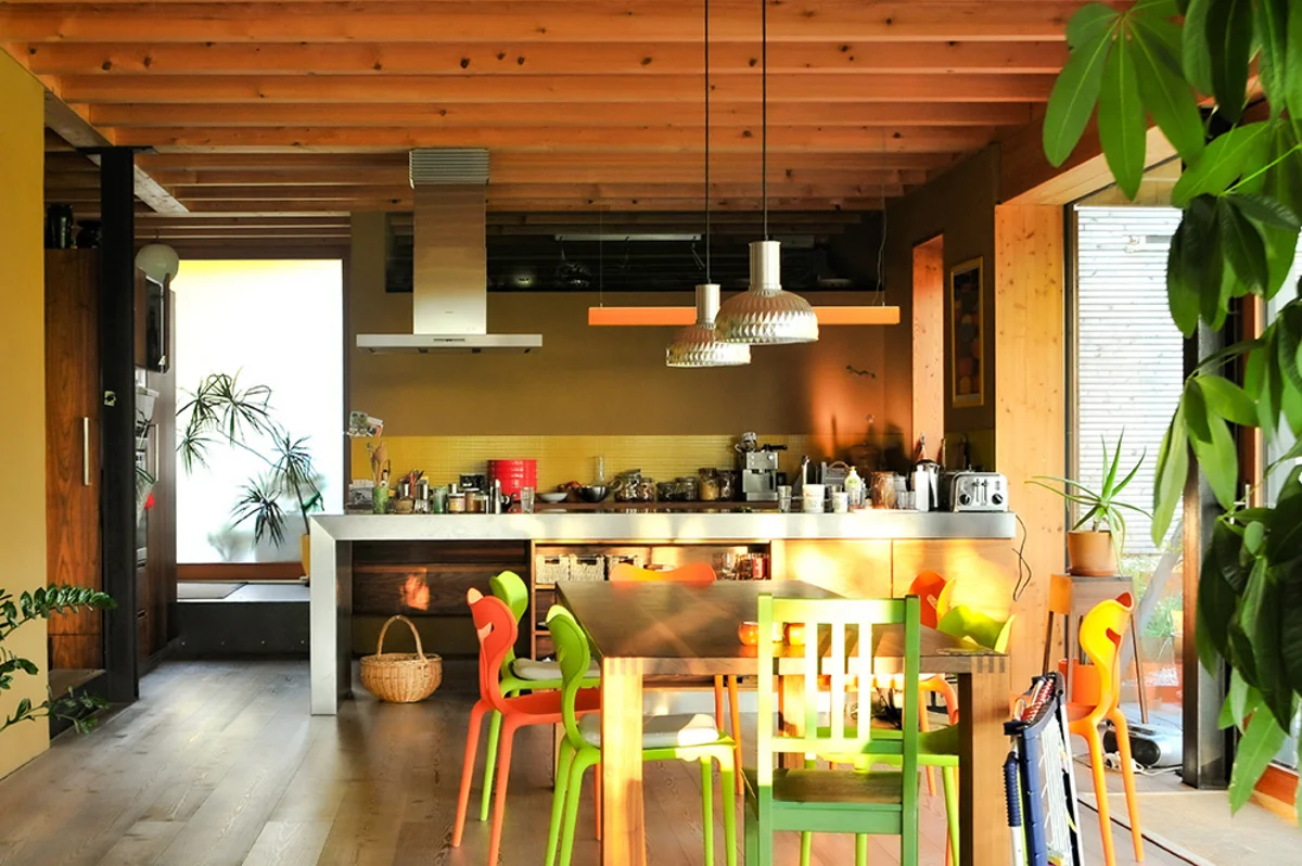 Offener Ess- und Küchenbereich mit verschiedenen, bunten Stühlen und warmer Atmosphäre. Sichtholzbalkendecke eines Massivholzhauses. © Brunthaler Naturhausmanufaktur