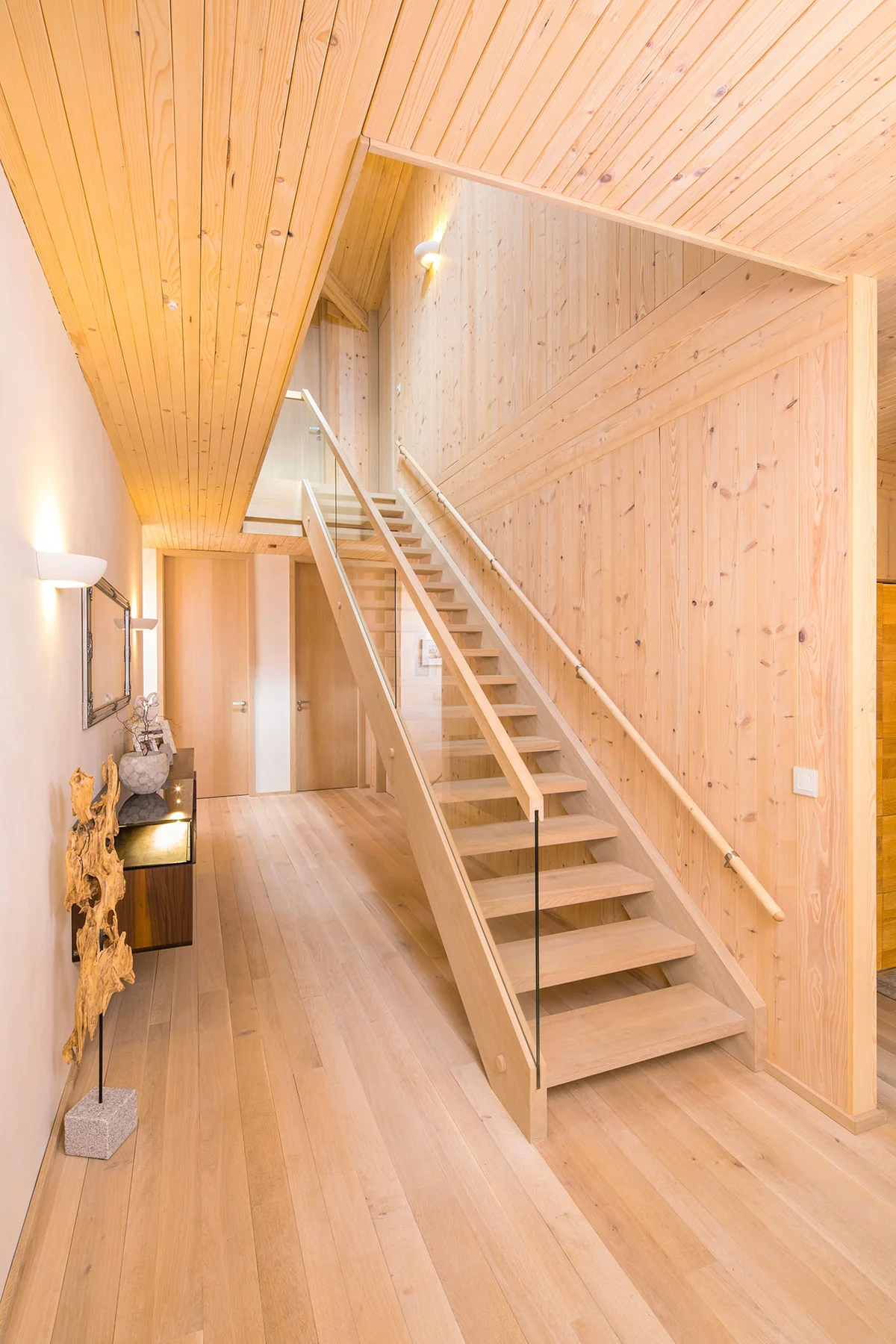 Moderne, helle Holztreppe mit Holz-Glas-Geländer und Massivholzwand. Massivholzdecke, Holztüren. © Brunthaler Naturhausmanufaktur