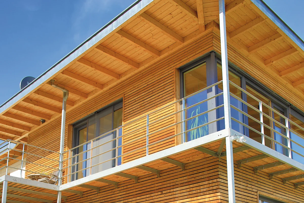 Detailaufnahme und Untersicht des Dachüberstands. Die großen Balkontüren laufen teilweise über Eck. Hellgrauen Streben stützen den Balkon und ein minimalistisches Geländer komplettiert diesen. © Brunthaler Naturhausmanufaktur