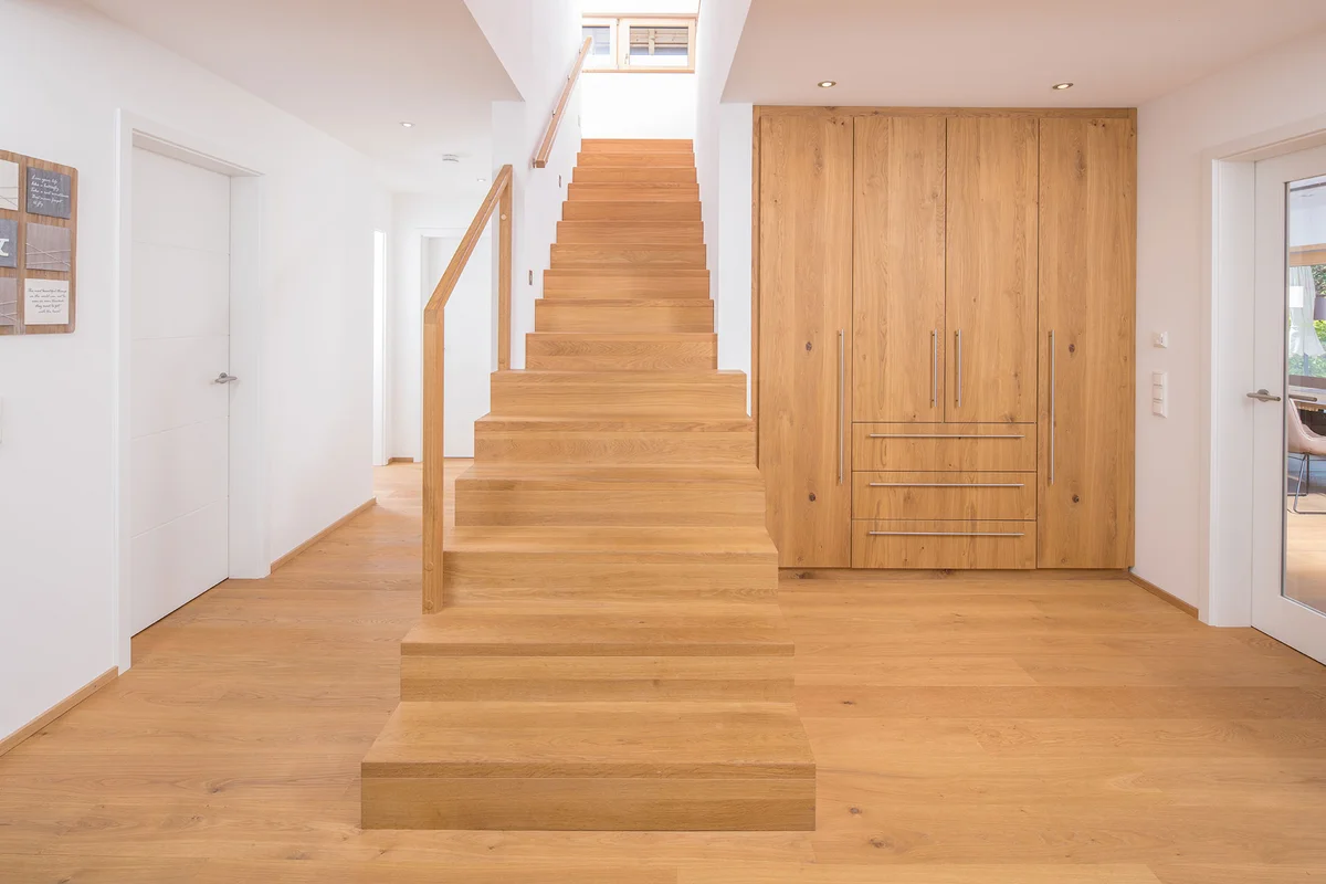 Holztreppe, Holzfußboden und die Schrankwand in identischem Holz geben einen warmen Kontrast zu den weiß verputzten Wänden im Holzhaus. © Brunthaler Naturhausmanufaktur