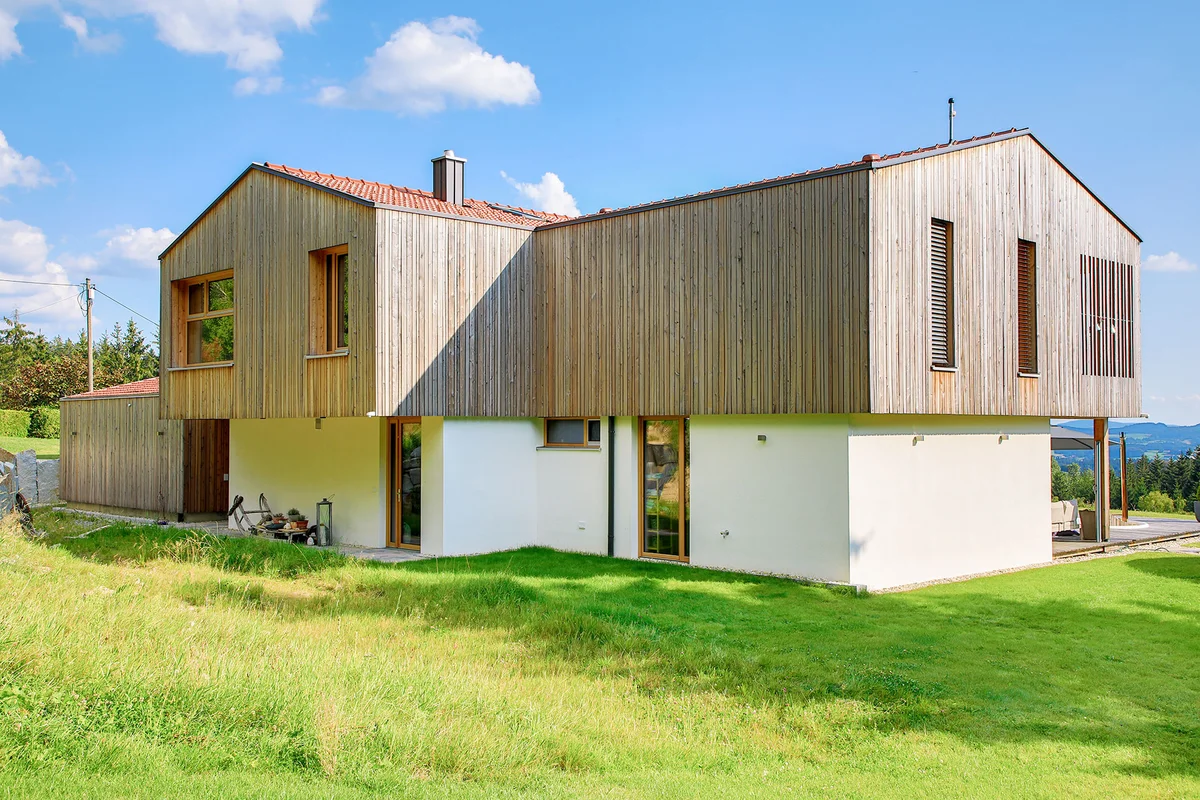 Rückansicht eines modernen kastenförmigem Architektenholzhaus mit Überhang des oberen Stockwerks. Vertikale Holzfassade und verputzte Fassade im Erdgeschoss. © Brunthaler Naturhausmanufaktur