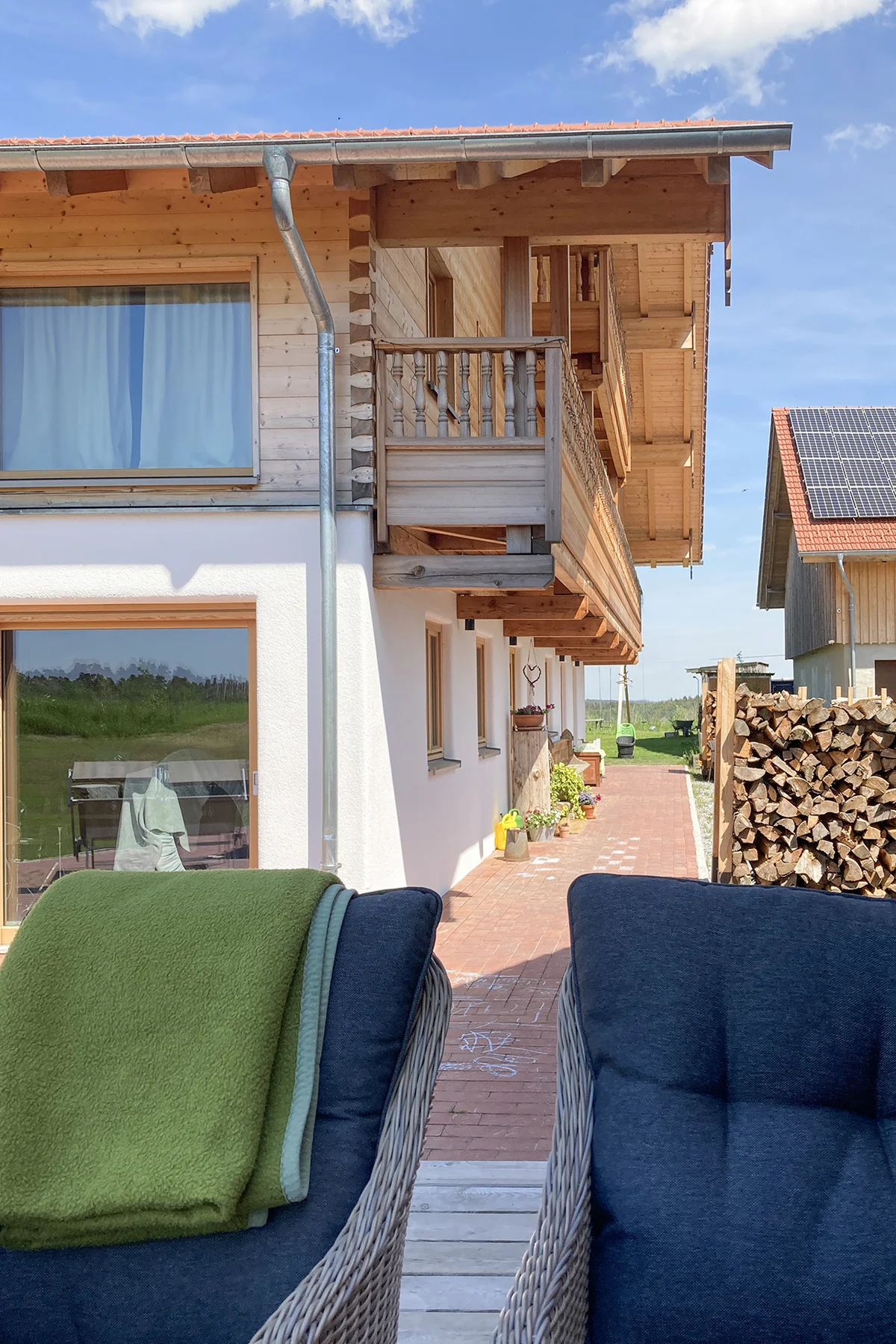 Seitenansicht eines bayerischen Landhauses mit urigem Holzbalkon und Blockbohlenfassade. Das untere Stockwerk ist verputzt. © Brunthaler Naturhausmanufaktur
