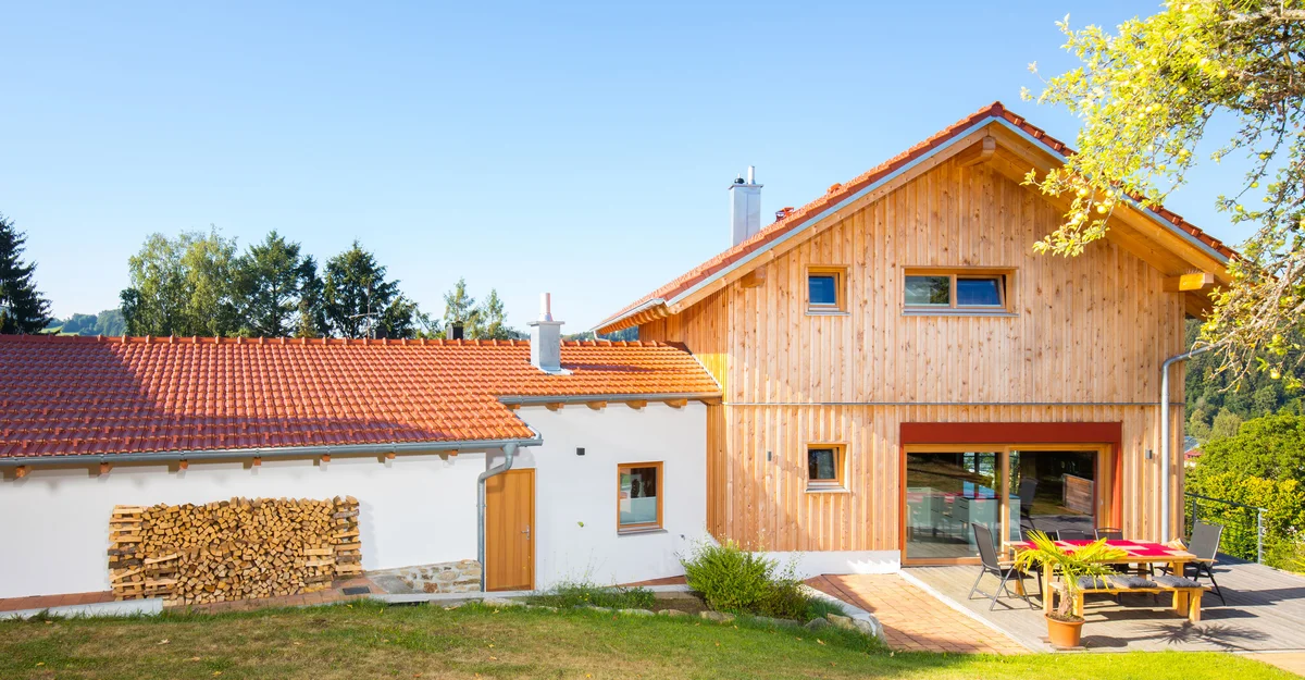 Holzhaus mit vertikaler Holzfassade, roten Farbakzenten und einer Garage mit verputzter Fassade. © Brunthaler Naturhausmanufaktur