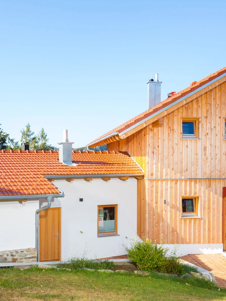 Holzhaus mit vertikaler Holzfassade, roten Farbakzenten und einer Garage mit verputzter Fassade. © Brunthaler Naturhausmanufaktur