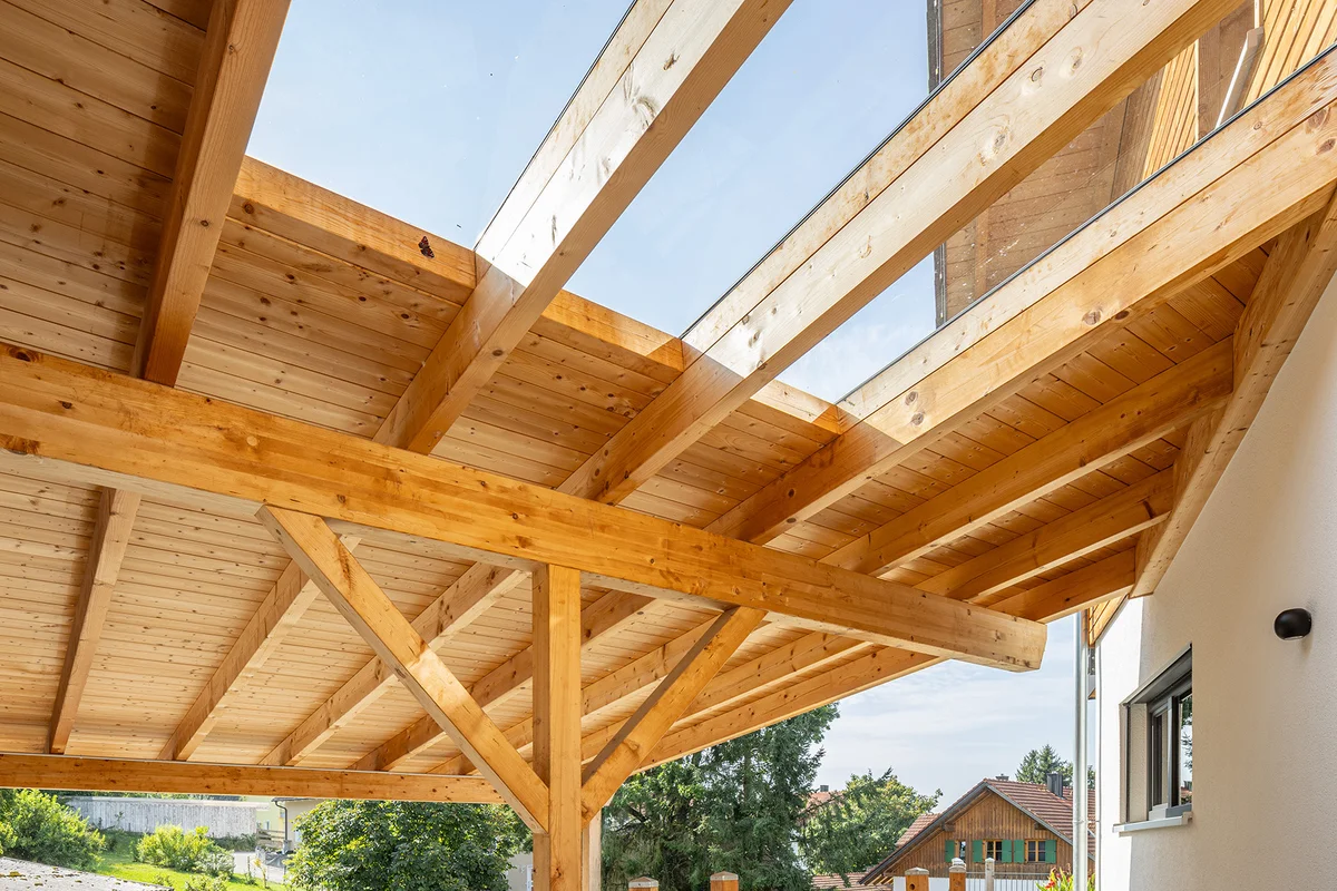 Überdachung eines Holzhauses für den Außenbereich und Carport. Die Überdachung ist aus Massivholz und hat ein paar große Dachfenster aus Glas für mehr Helligkeit. © Brunthaler Naturhausmanufaktur