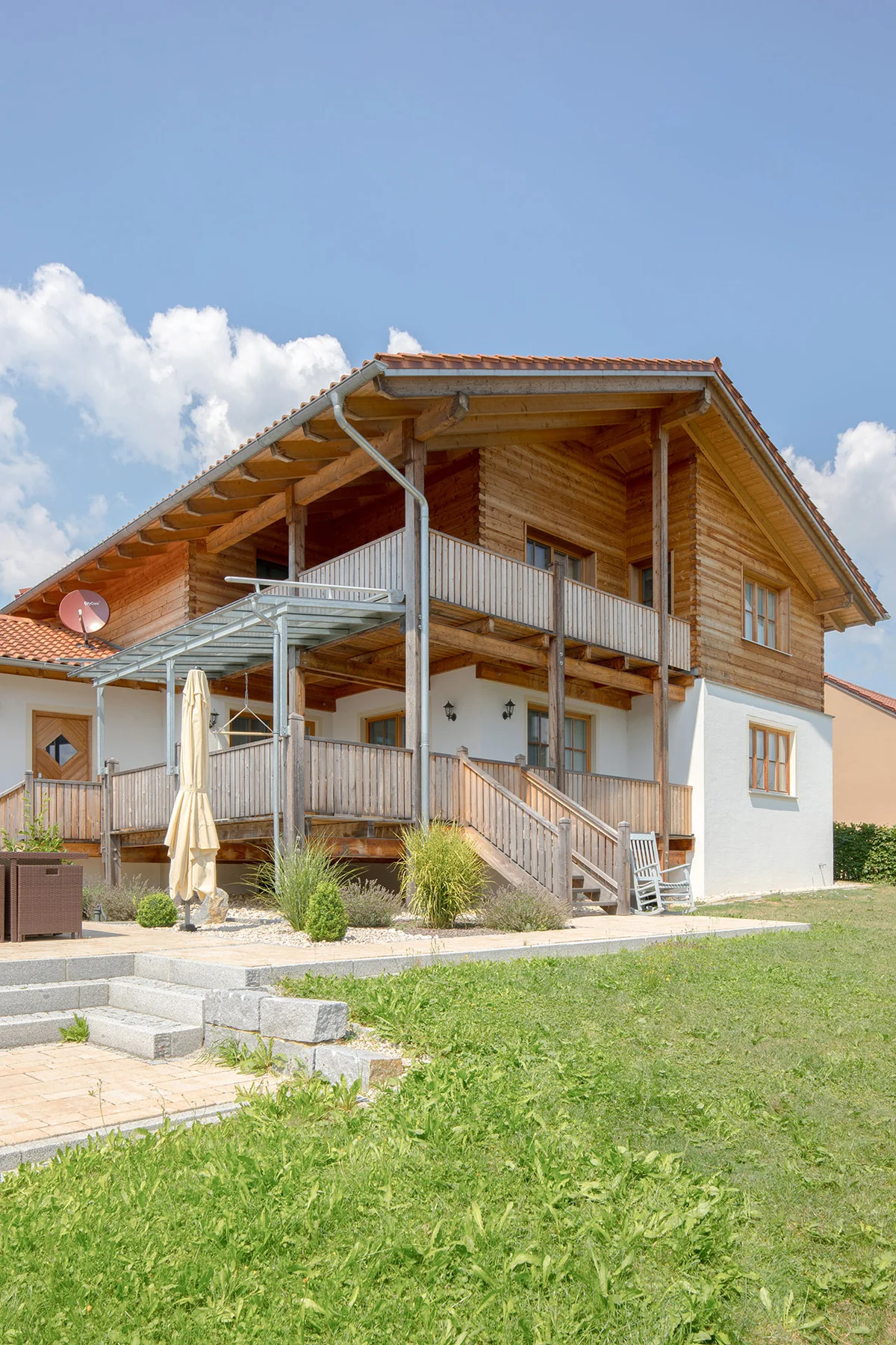 Großes Massivholz-Landhaus mit Blockbohlenfassade oben und verputzter Fassade im Erdgeschoss. Eine erhöhte aufgeständerte Holzterrasse und der Holzbalkon ermöglichen eine gute Sicht auf den Garten. © Brunthaler Naturhausmanufaktur