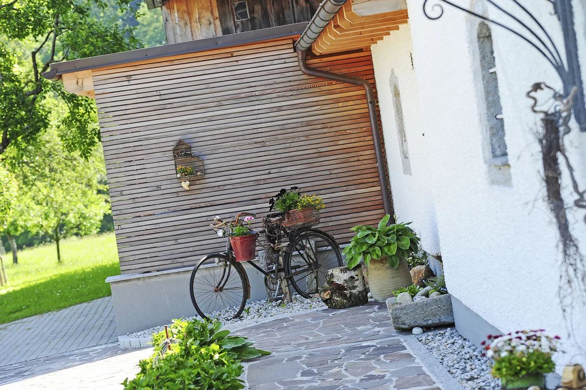 Ein altes Fahrrad mit Blumen steht als dekoratives Element vor der verputzten Fassade eines Innviertler Hofs. © Brunthaler Naturhausmanufaktur