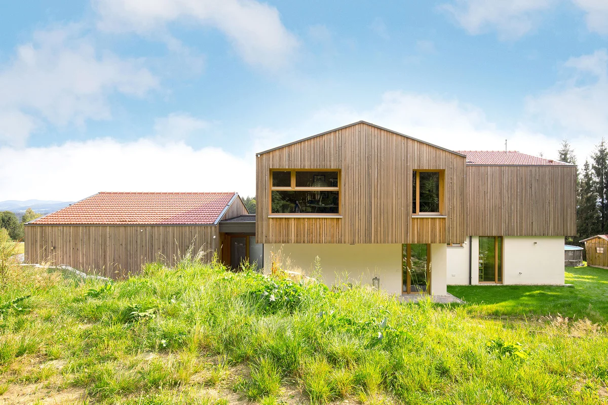 Rückansicht eines modernen kastenförmigem Architektenholzhaus mit Überhang des oberen Stockwerks. Vertikale Holzfassade und verputzte Fassade im Erdgeschoss. © Brunthaler Naturhausmanufaktur