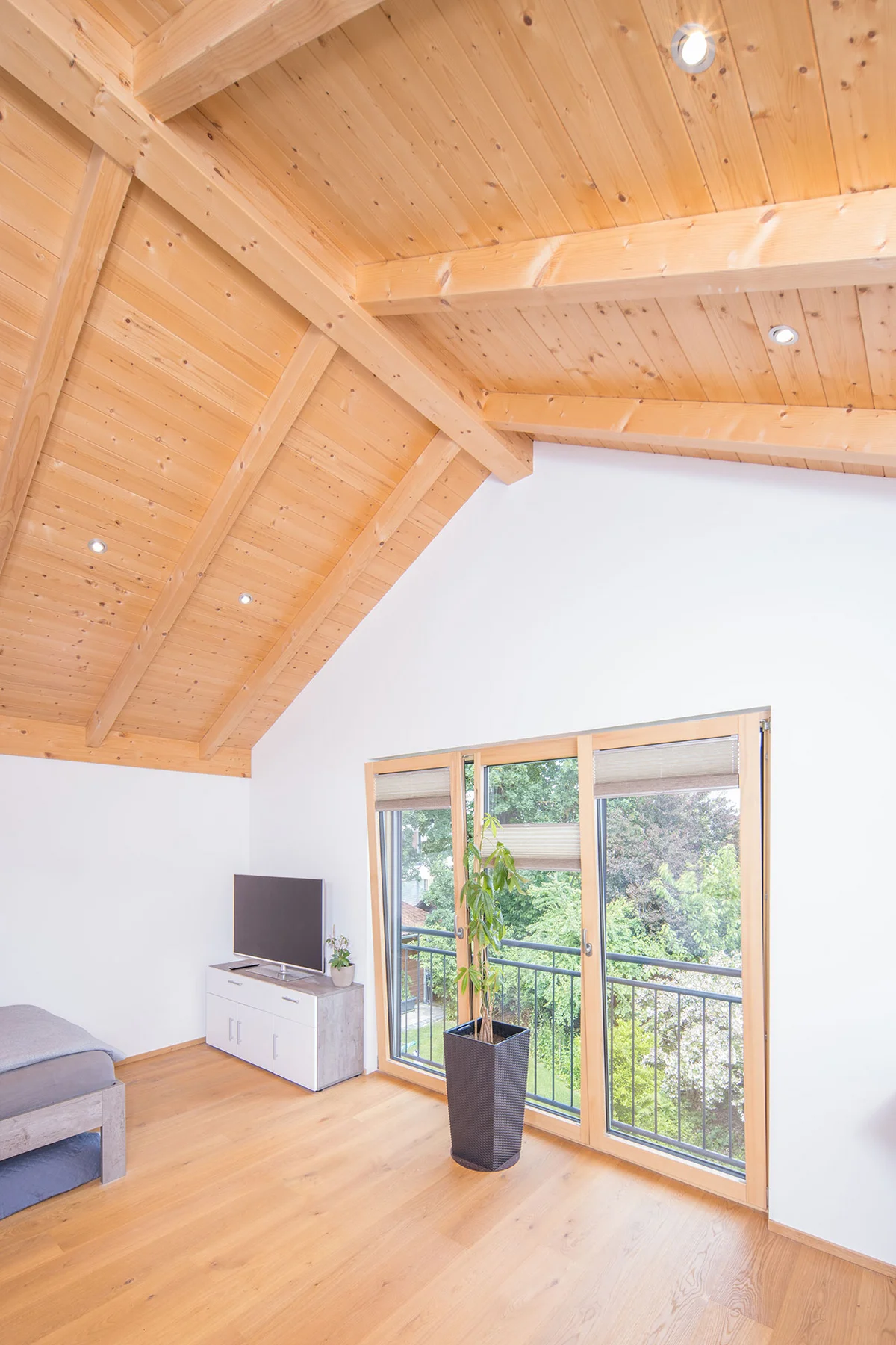 Dachgeschoss mit Sichtdachstuhl und verputzten Holzwänden. In der Wand sind bodentiefe Balkontüren mit einem Stahlgeländer. In die Decke sind Licht-Spots eingearbeitet. © Brunthaler Naturhausmanufaktur