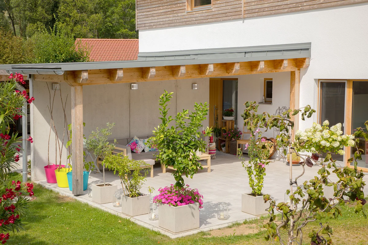 Detailaufnahme der überdachten Terrasse mit hellgrauer Couch, vielen Pflanzen, die die Terrasse umsäumen. © Brunthaler Naturhausmanufaktur