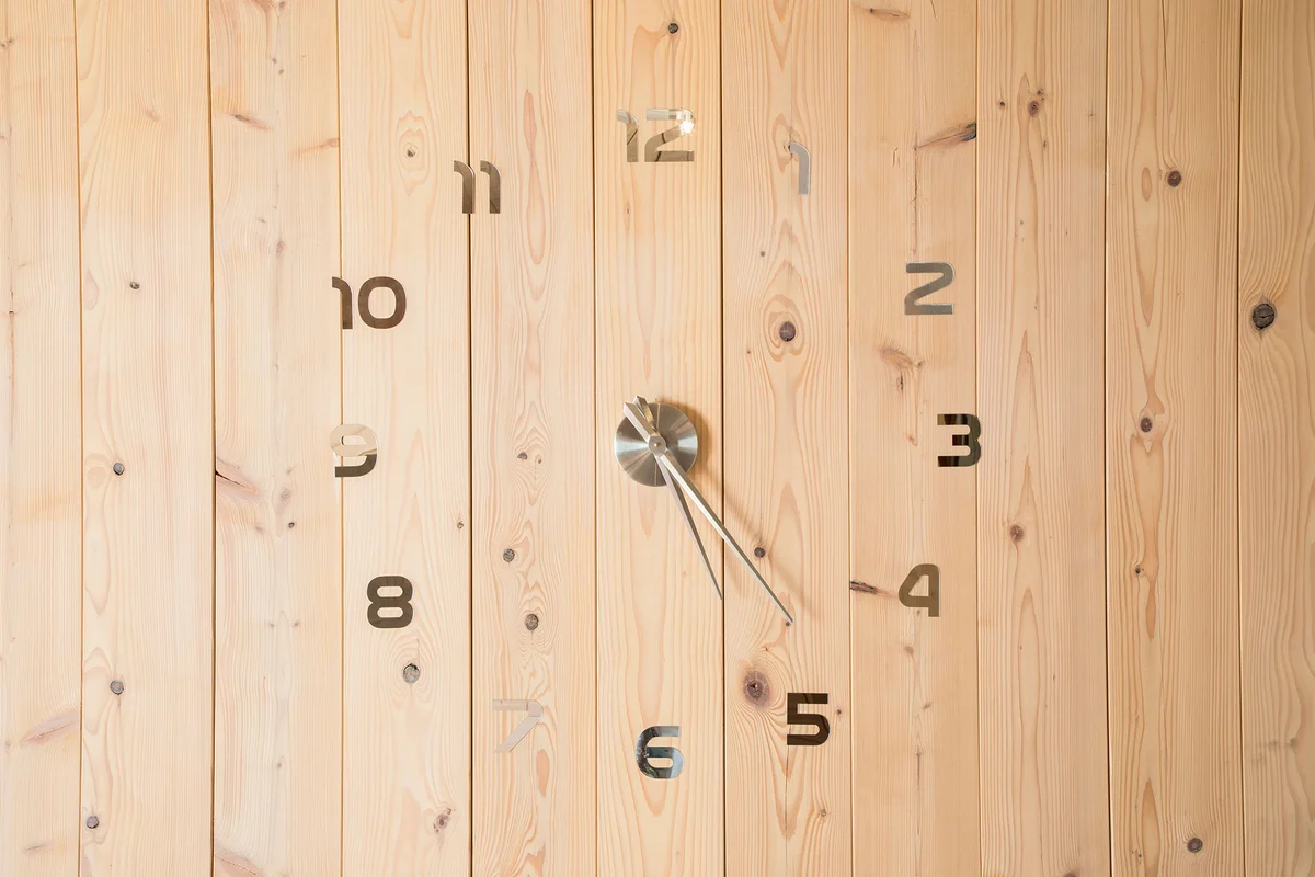 Detailaufnahme einer Wanduhr, die minimalistisch nur als Ziffern und Zeiger an die Holzwand montiert wurde. © Brunthaler Naturhausmanufaktur