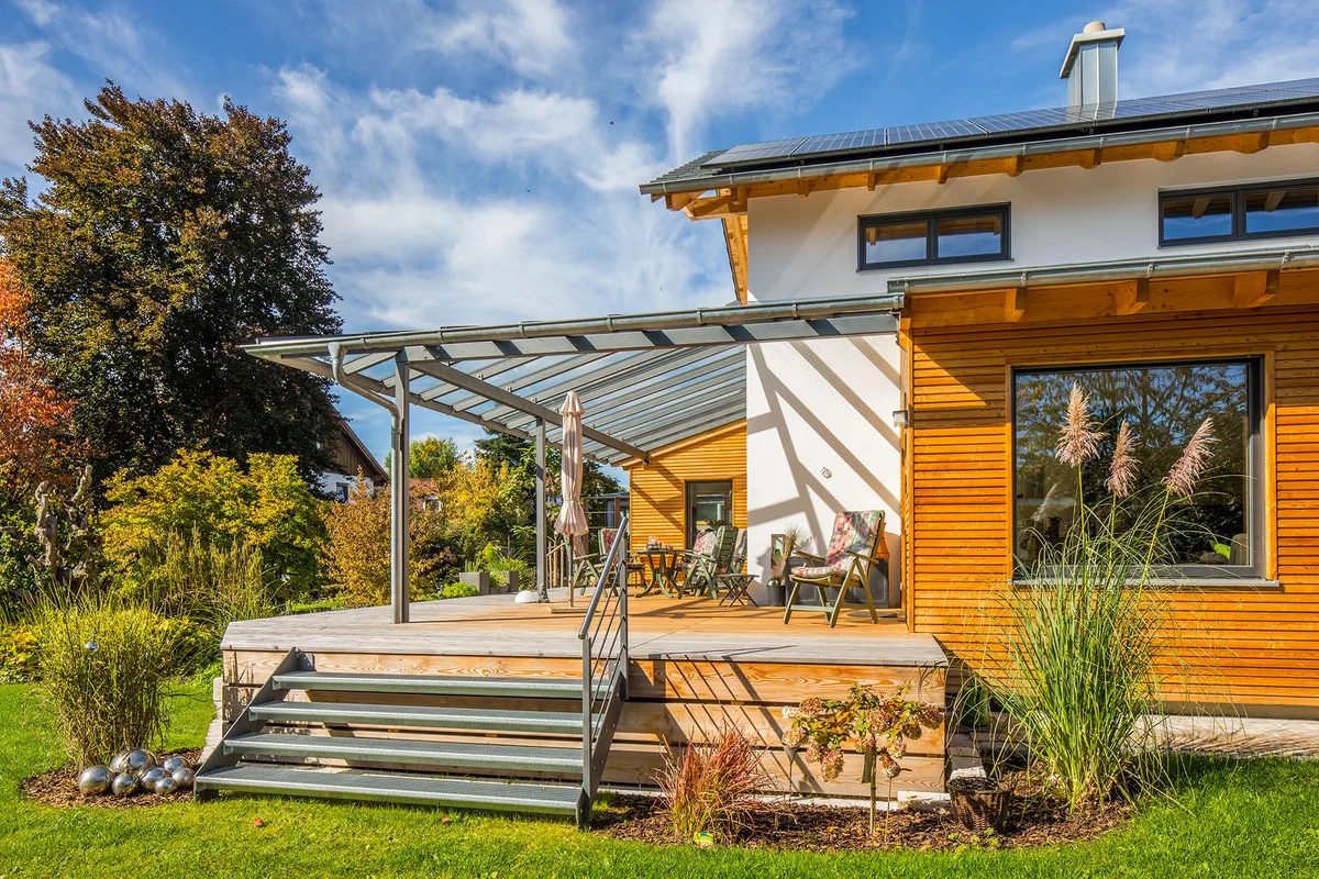 Das Holzhaus ist teilweise verputzt und hat einen überdachten Übereck-Erker mit einer horizontalen Holzfassade. Auf der anderen Seite ist eine überdachte Terrasse. © Brunthaler Naturhausmanufaktur