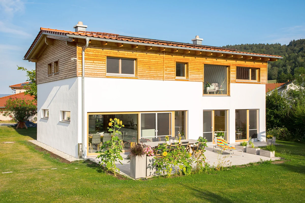 Klassisches Einfamilienhaus mit verputzter Fassade und einem kleinen Teil an horizontaler Holzfassade. Viele große Fenster und eine betonierte Terrasse ergänzen das Holzhaus. © Brunthaler Naturhausmanufaktur