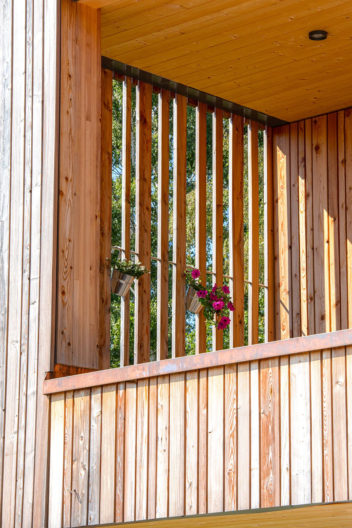 Detailaufnahme eines Holzbalkons mit vertikaler Holzfassade, die teils als Sonnenschutz fungiert. © Brunthaler Naturhausmanufaktur