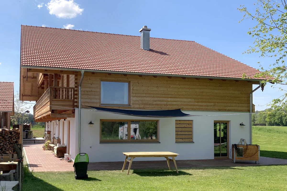 Seitenansicht des bayerischen Landhauses mit Sonnensegel. Das Dach hat einen starken Überhang nach vorne um den Holzbalkonen eine Überdachung zu bieten. © Brunthaler Naturhausmanufaktur