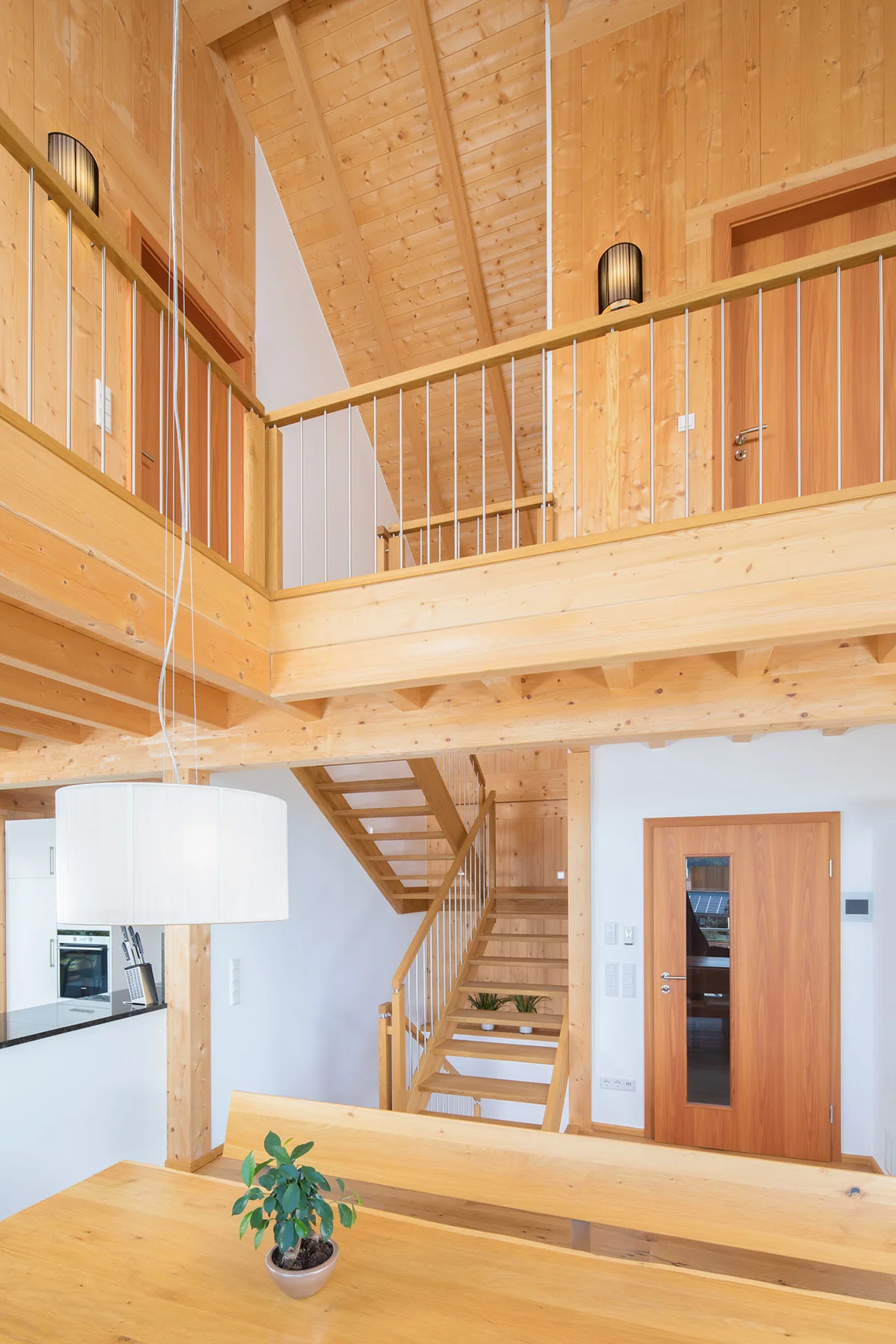 Eine Galerie im Wohnhaus, mit Sicht von unten aus dem Essbereich nach oben zu den Schlafzimmern. Man sieht viele Holzwände und das Geländer der Galerie. © Brunthaler Naturhausmanufaktur