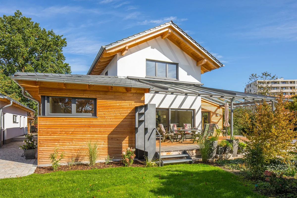 Das Holzhaus ist teilweise verputzt und hat einen überdachten Übereck-Erker mit einer horizontalen Holzfassade. Auf der anderen Seite ist eine überdachte Terrasse. © Brunthaler Naturhausmanufaktur