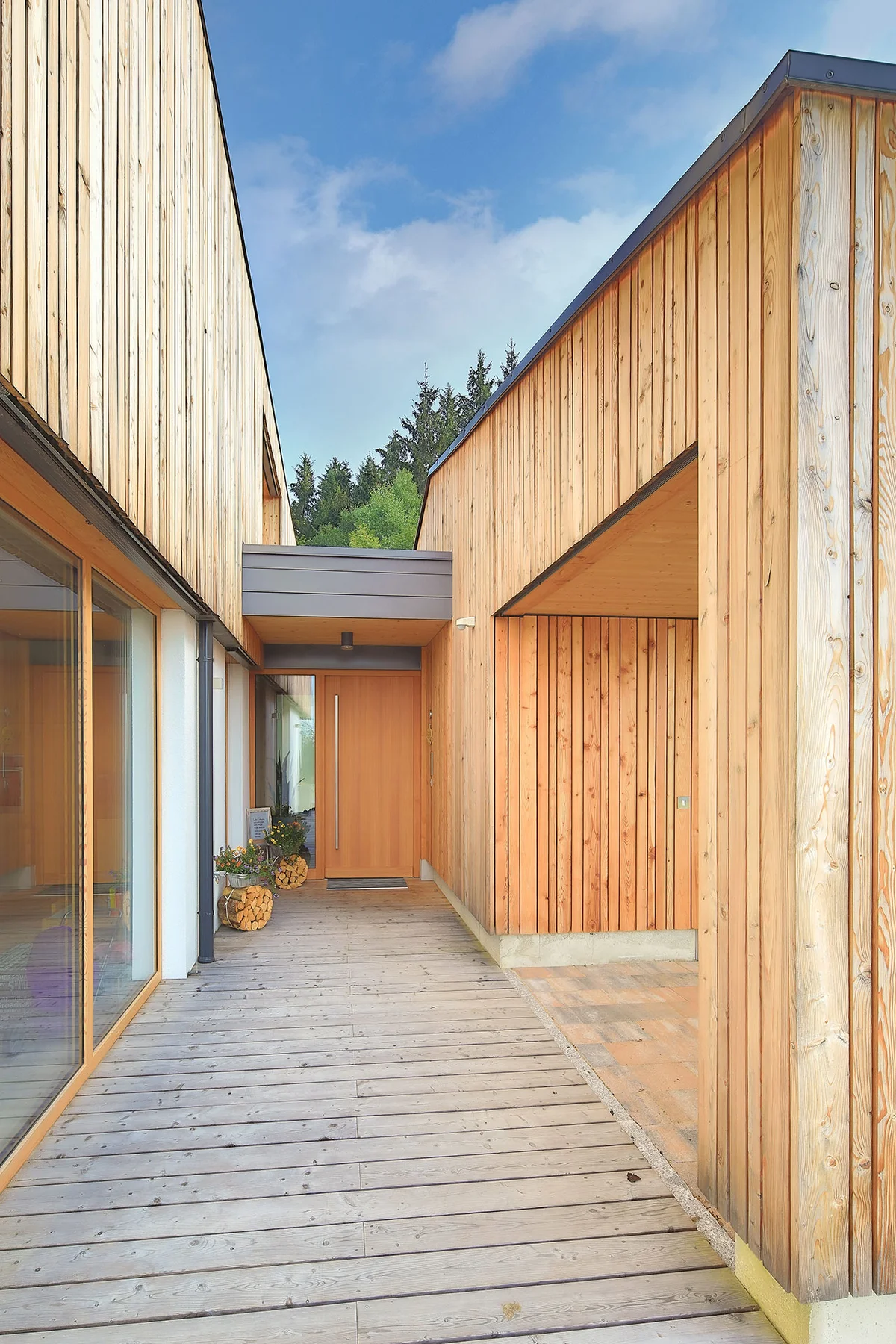 Eingangsbereich als Verbindung zwischen Garage und Haus. Das Architektenholzhaus hat eine vertikale helle Holzfassade und ein verputztes Erdgeschoss. © Brunthaler Naturhausmanufaktur