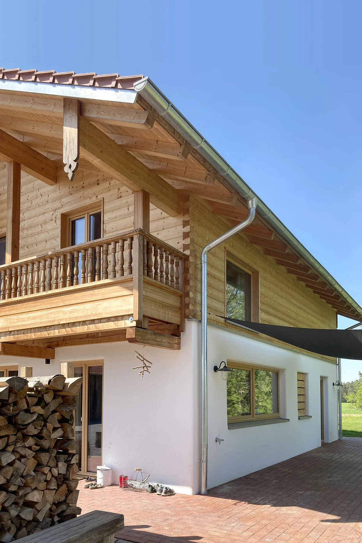 Detailaufnahme eines Holzhauses. Man sieht das Eck des Hauses mit einem Teil des Holzbalkons vorne und einer weiteren Außenseite des bayerischen Landhauses. © Brunthaler Naturhausmanufaktur