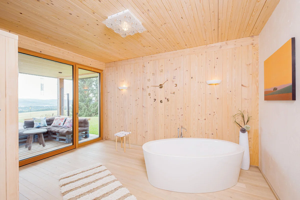 Badezimmer komplett aus Holz mit frei stehender großer ovaler Badewanne. Der Raum hat eine bodenlange Terrassentür aus Glas. © Brunthaler Naturhausmanufaktur