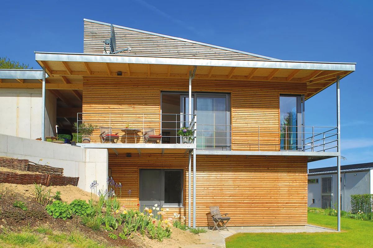 Seitliche Ansicht des modernen Holzhauses mit Pultdach und über Eck laufendem Balkon der durch die Hanglage mit dem Eingangsbereich verbunden ist. © Brunthaler Naturhausmanufaktur