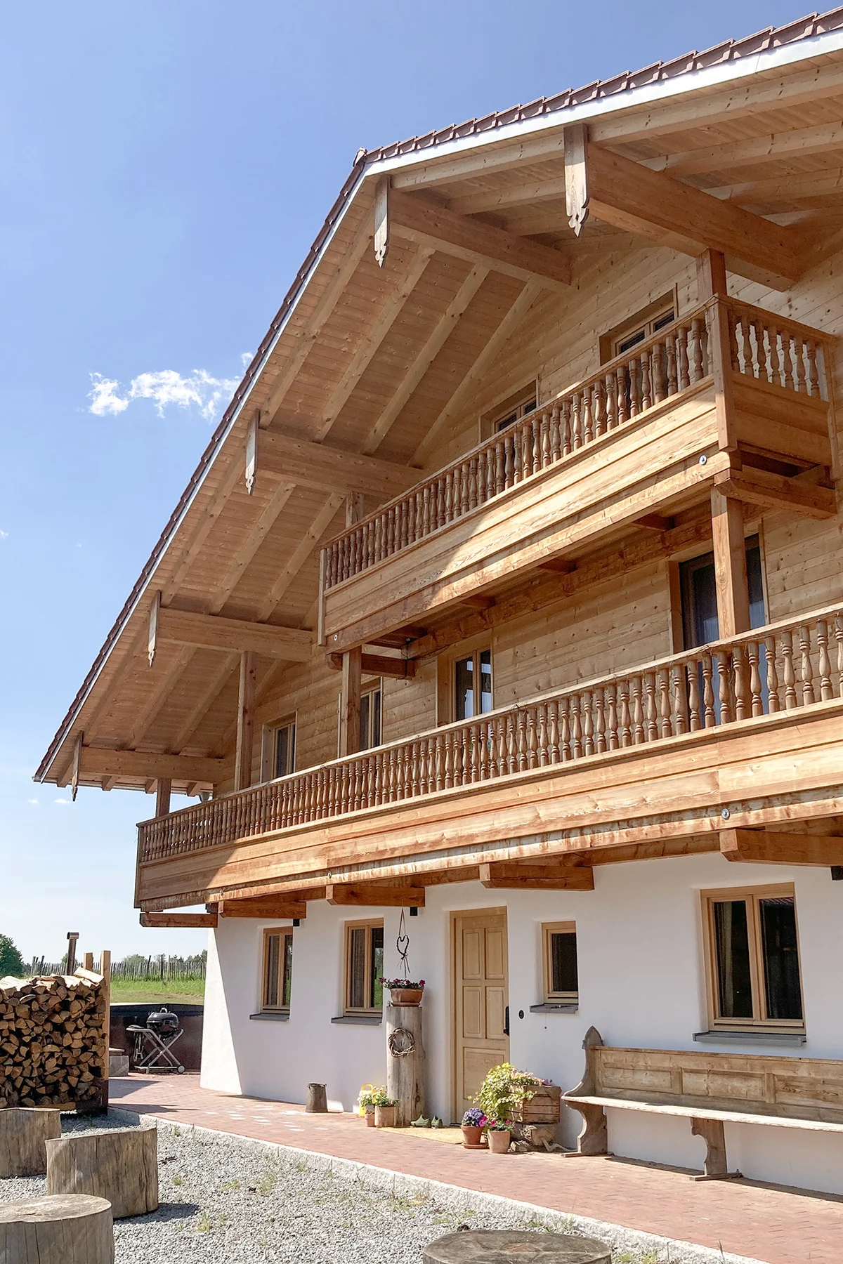 Vorderseite eines großen bayerischen Landhauses mit Blockbohlenfassade und dekorativen Pfettenbrettern. Das untere Stockwerk ist verputzt, darüber sind zwei große Balkone aus Holz. © Brunthaler Naturhausmanufaktur