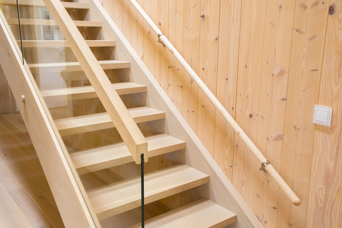Detailaufnahme einer minimalistischen Holztreppe vor einer Massivholzwand. © Brunthaler Naturhausmanufaktur