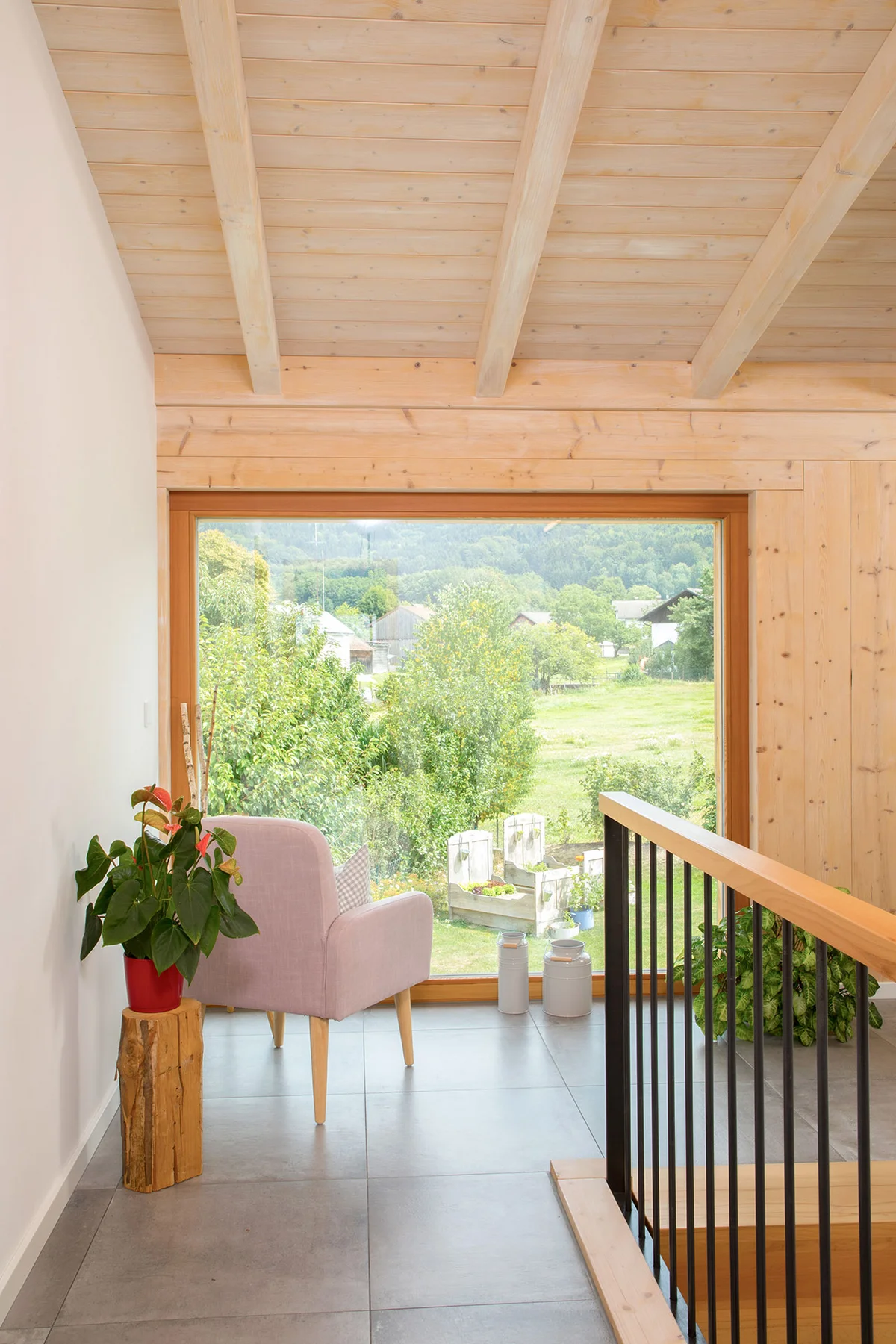 Flurbereich beim Treppenabgang mit einem großen bodentiefen Fenster und bequemen altrosa farbenem Sessel um in die Landschaft zu sehen. © Brunthaler Naturhausmanufaktur