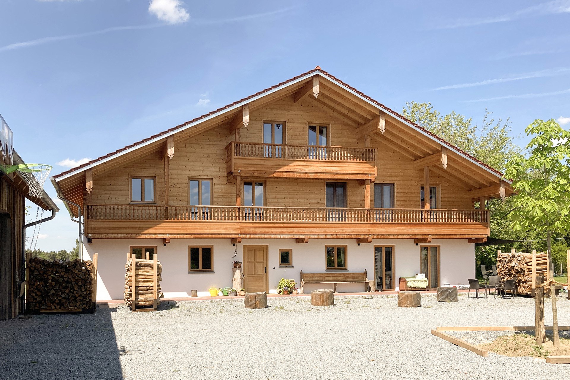 Großes bayerisches Landhaus. Teilweise weiß verputzt und oben mit rustikaler Blockbohlenfassade und zwei großzügigen Balkonen. © Brunthaler Naturhausmanufaktur