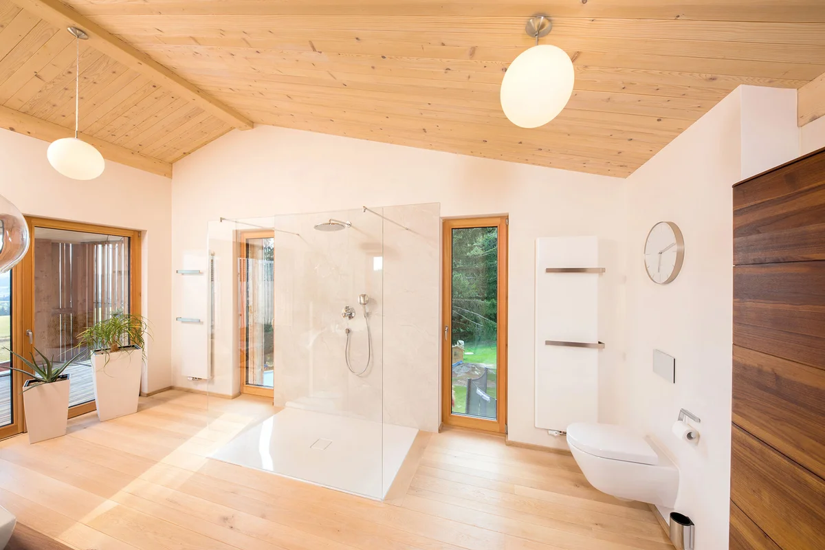 Badezimmer mit sehr großer üppiger moderner Dusche. Holzfußboden und Massivholzdecke, bodentiefe schmale Fenster. © Brunthaler Naturhausmanufaktur